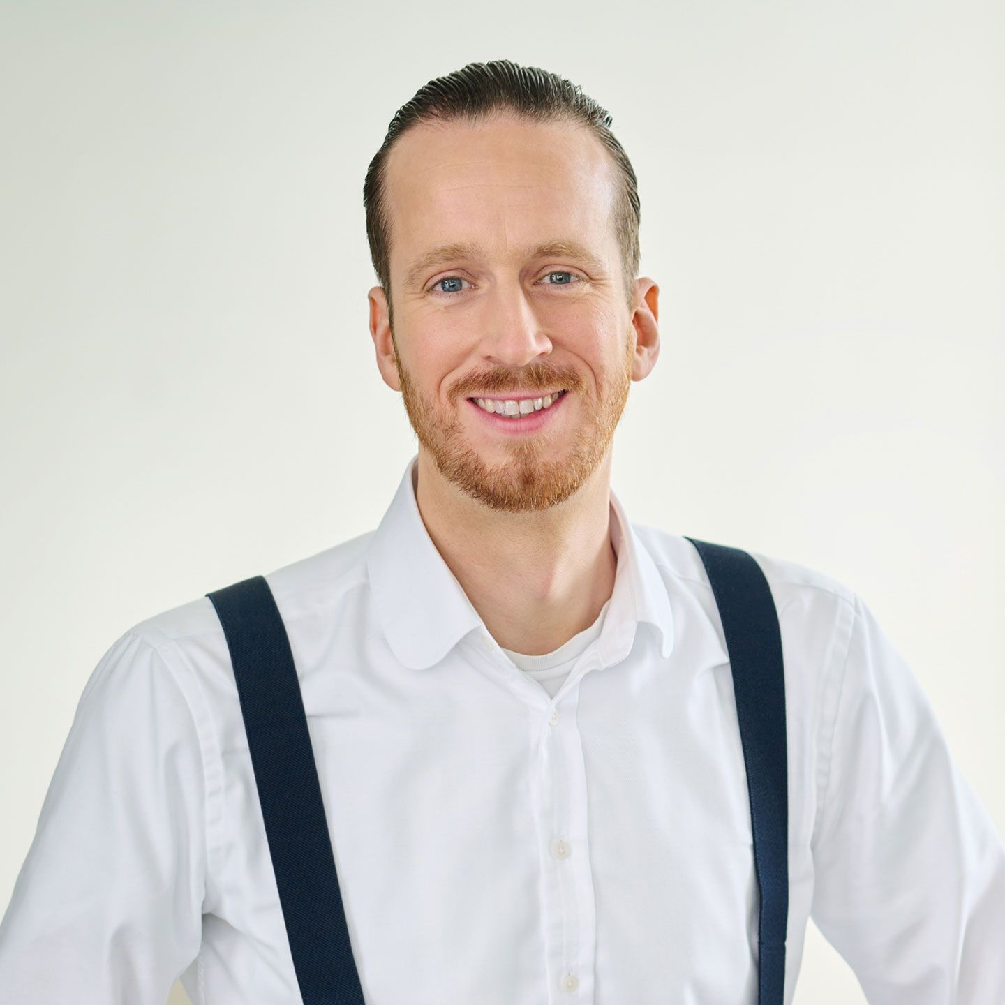 Sebastian Pollmer stojí v bílé košili s modrými šlemi ve světlé místnosti. 